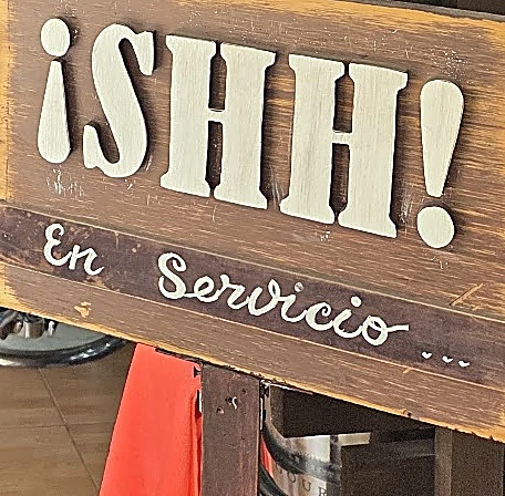 Cartel de madera con letras crema que dice ¡SHH! En servicio…