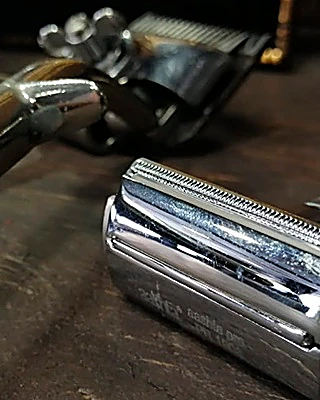 Navaja de barbero con mango de madera y rastrillo cromado sobre una mesa de madera oscura