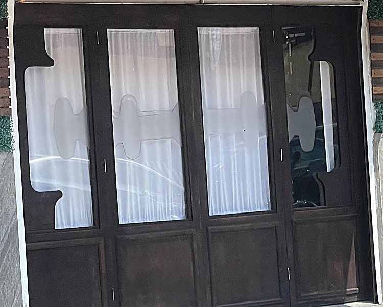 Puertas de madera oscura del local con vidrios esmerilados que tienen siluetas de navaja y peine